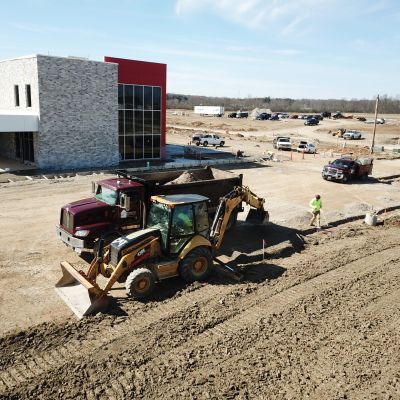 A dump truck and backhoe sit in front of a newly constructed commercial building