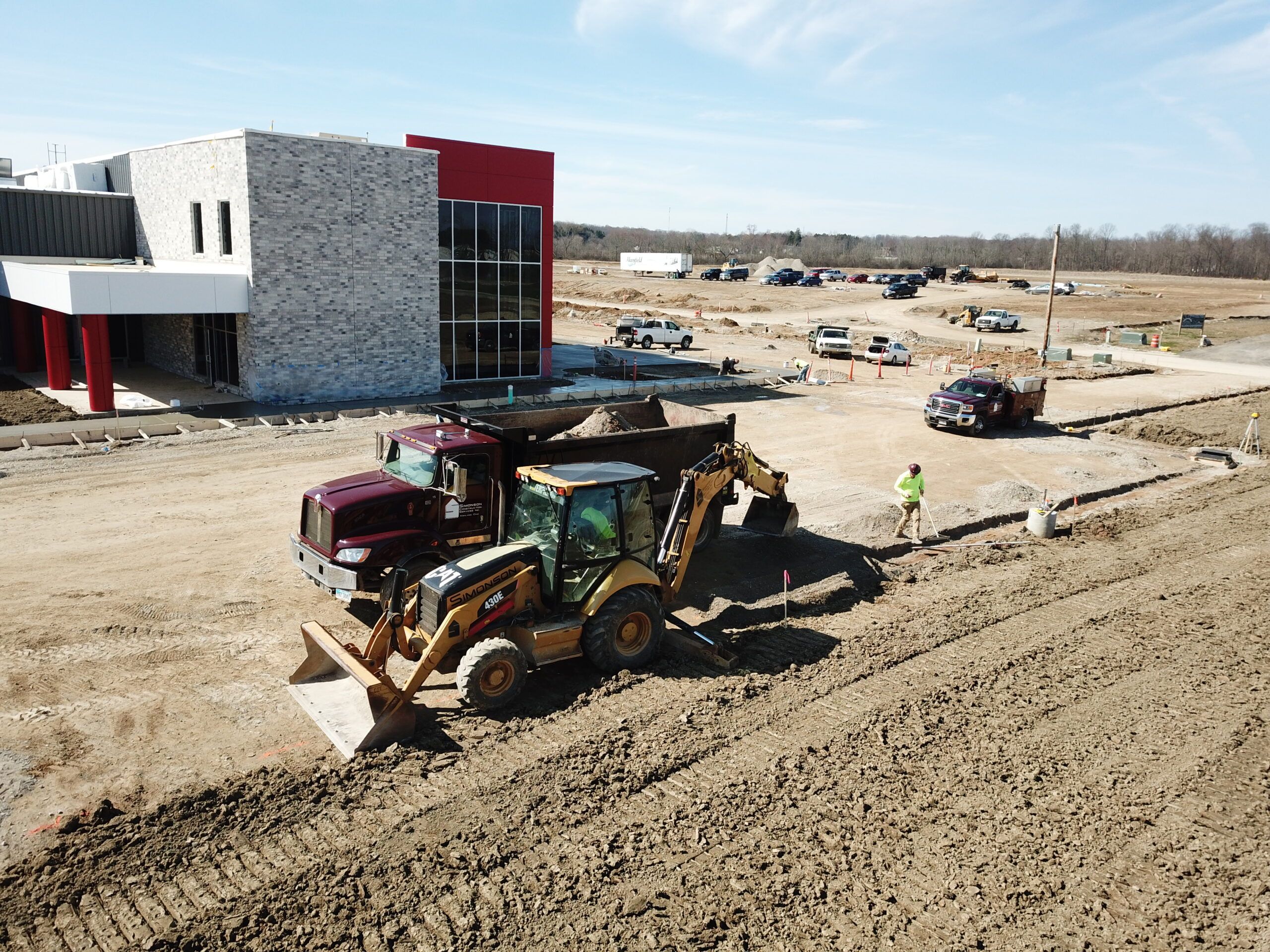 A dump truck and backhoe sit in front of a newly constructed commercial building