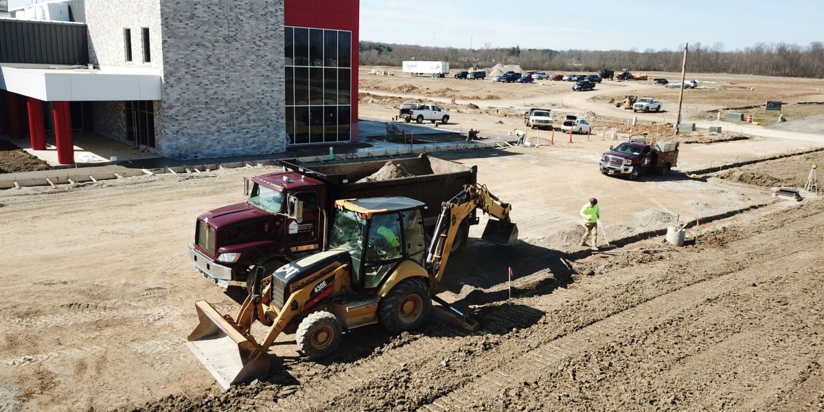 A dump truck and backhoe sit in front of a newly constructed commercial building