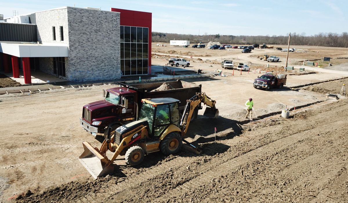 A dump truck and backhoe sit in front of a newly constructed commercial building