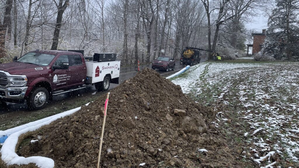 A utility truck, SUV, and hydro excavation truck line the side of the road during a watermain installation project